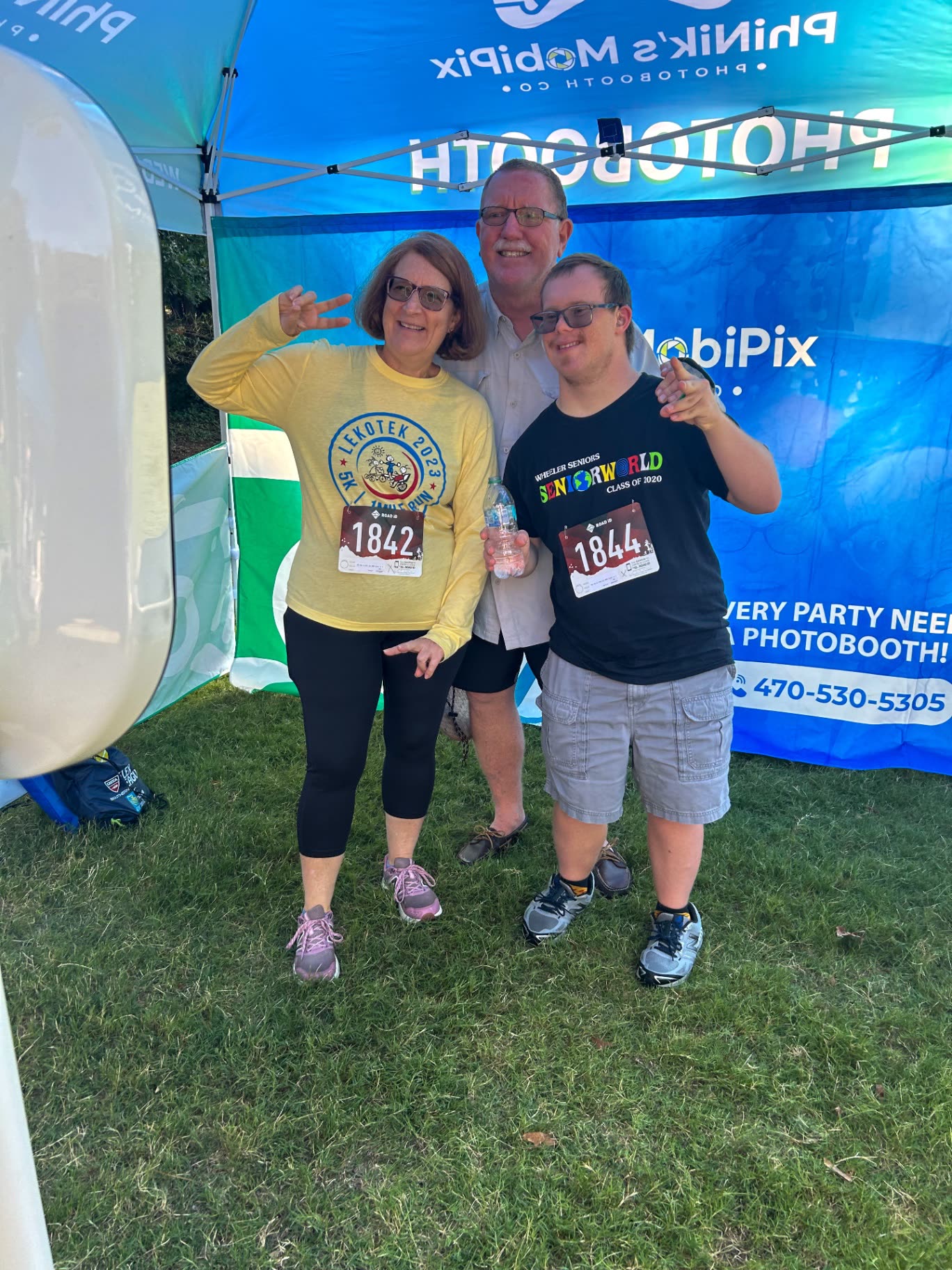 Family posing under the PhiNik's MobiPix photo booth tent at the Lekotek 5K