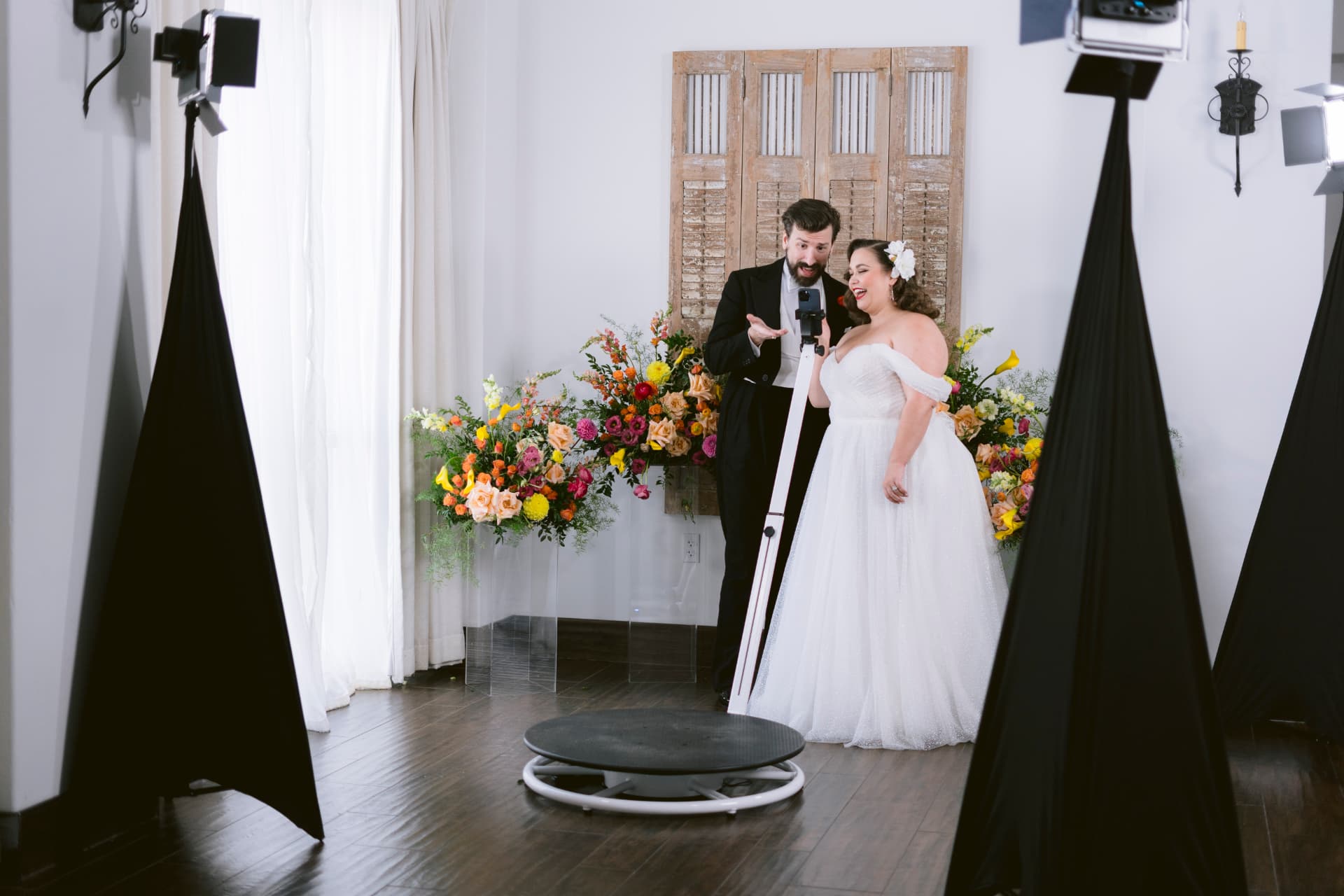 Bride and groom stepping onto the 360 video booth platform beside a floral arrangement