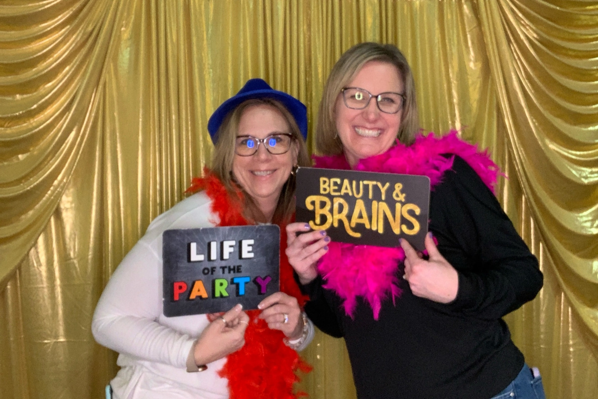 Two guests holding fun signs at the open-air booth with a gold backdrop