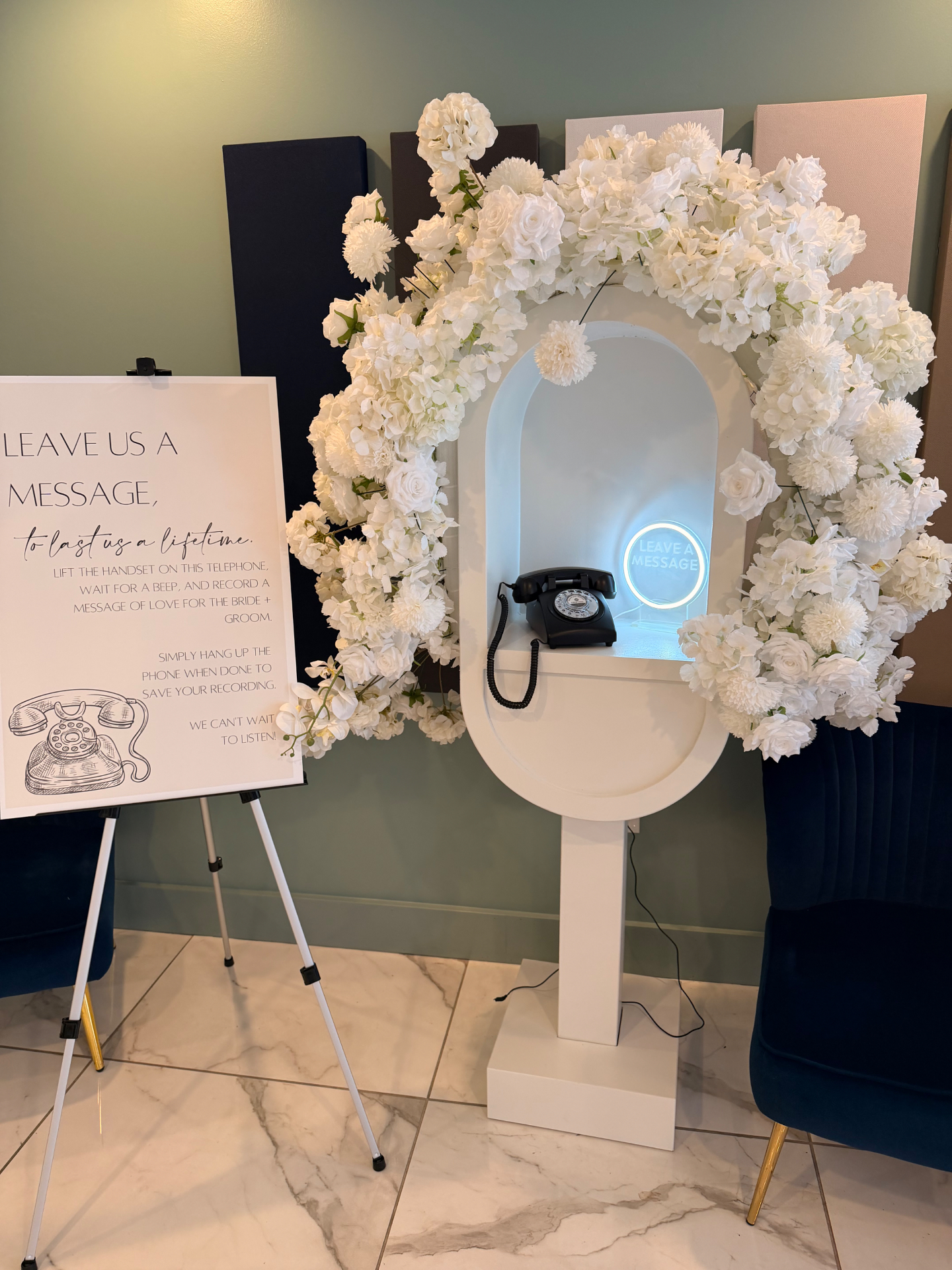 White arch audio guestbook booth framed with white florals and a Leave Us A Message sign
