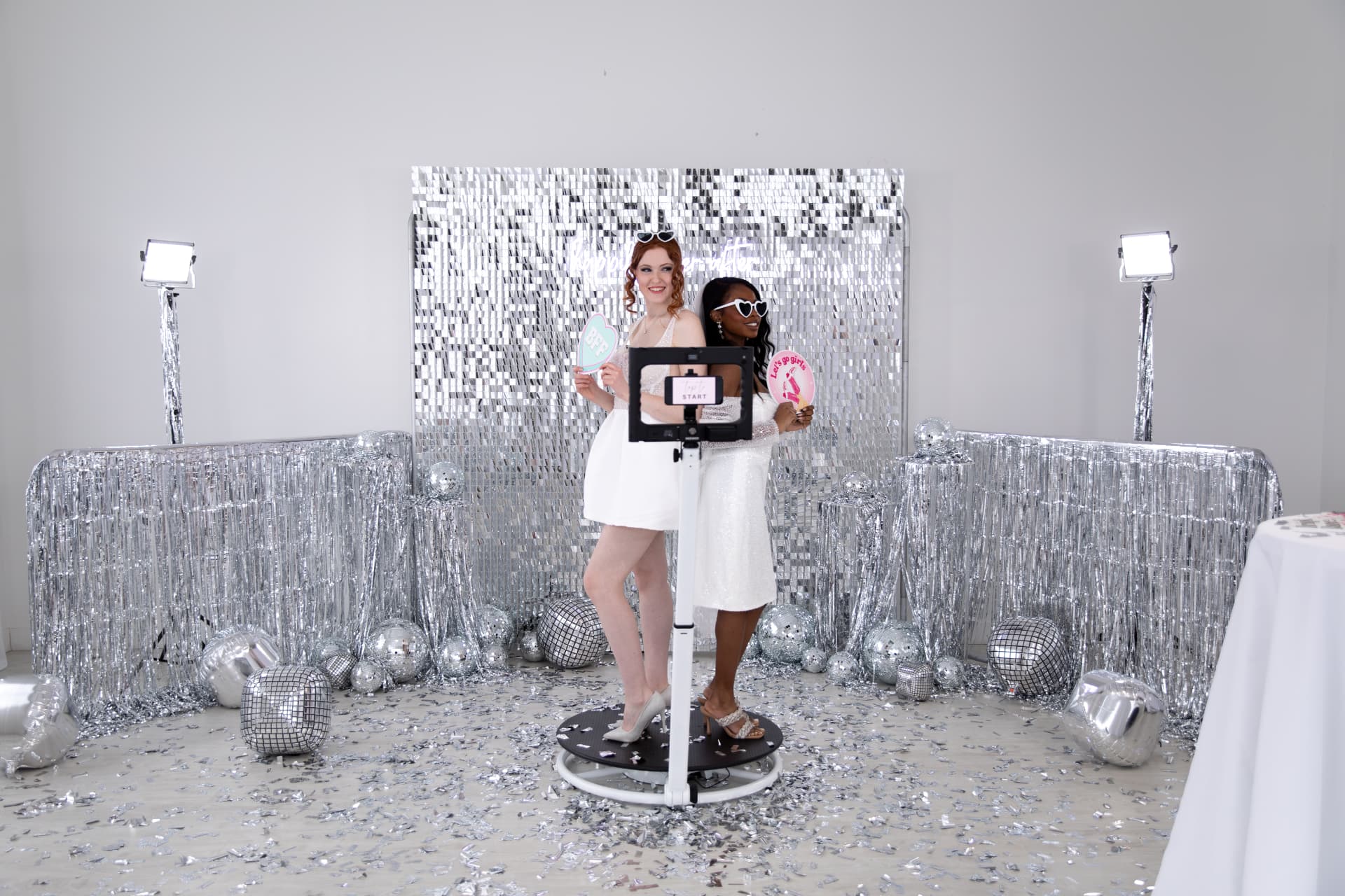 Two guests posing with props on the 360 video booth platform with disco backdrop