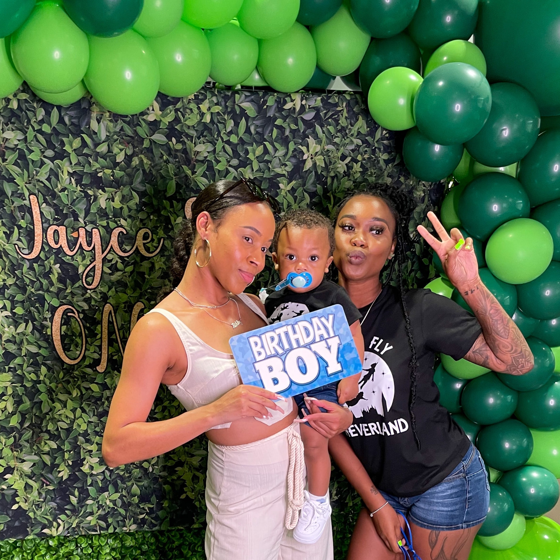 Birthday boy posing beside a greenery photo booth backdrop