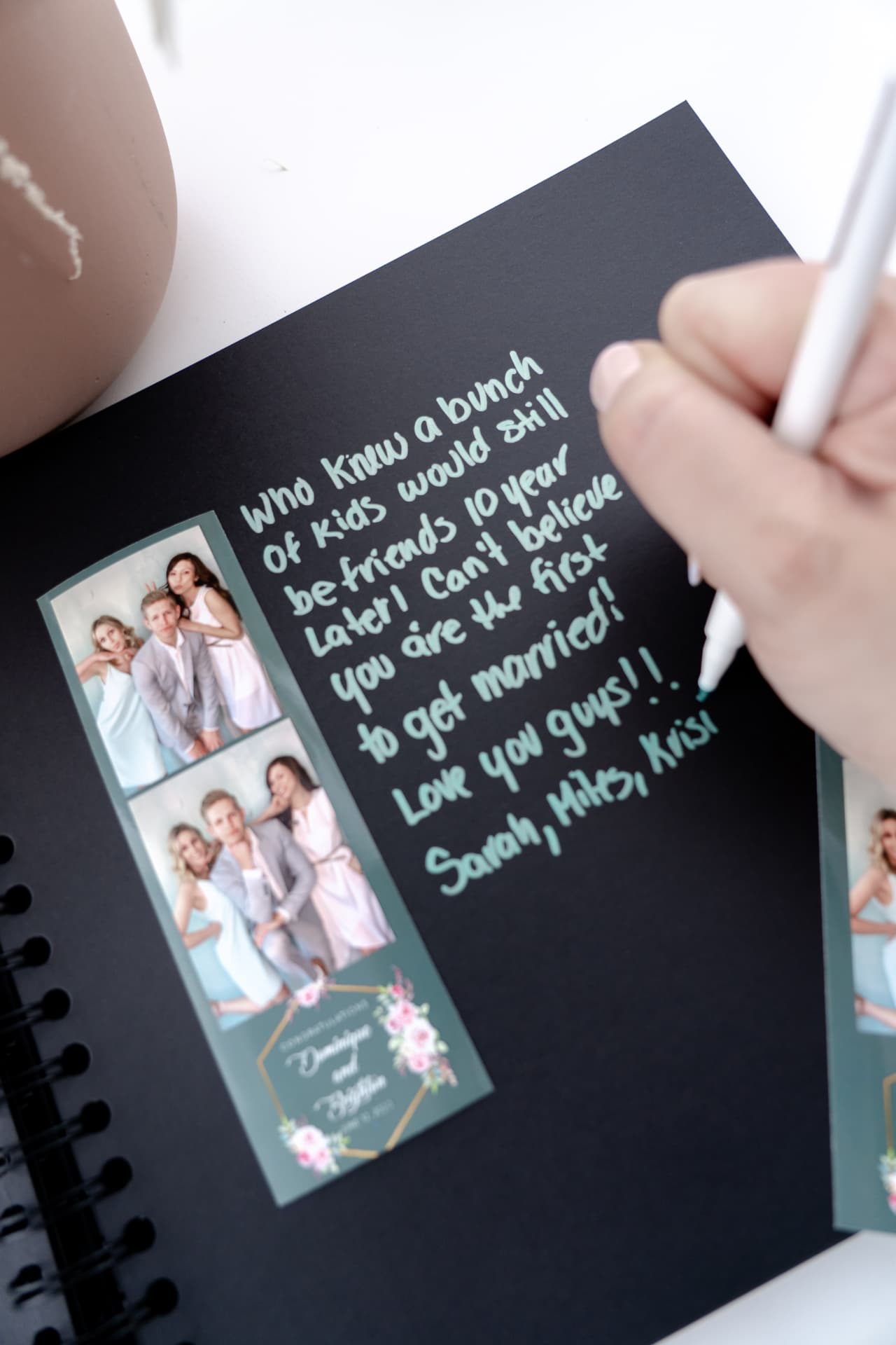 Guest writing a handwritten message beside photo strips in a black keepsake guest book album